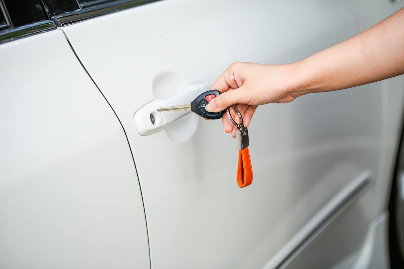 Hand holding car key and fob near white vehicle door ready to unlock it