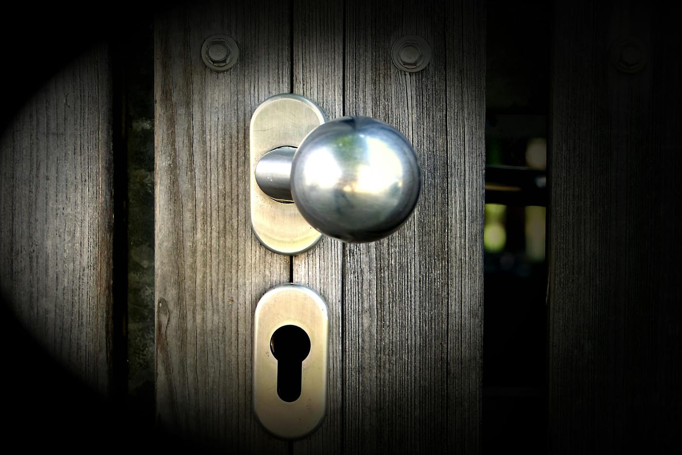 Silver door knob and deadbolt cylinder on weathered wooden door showing hardware detail