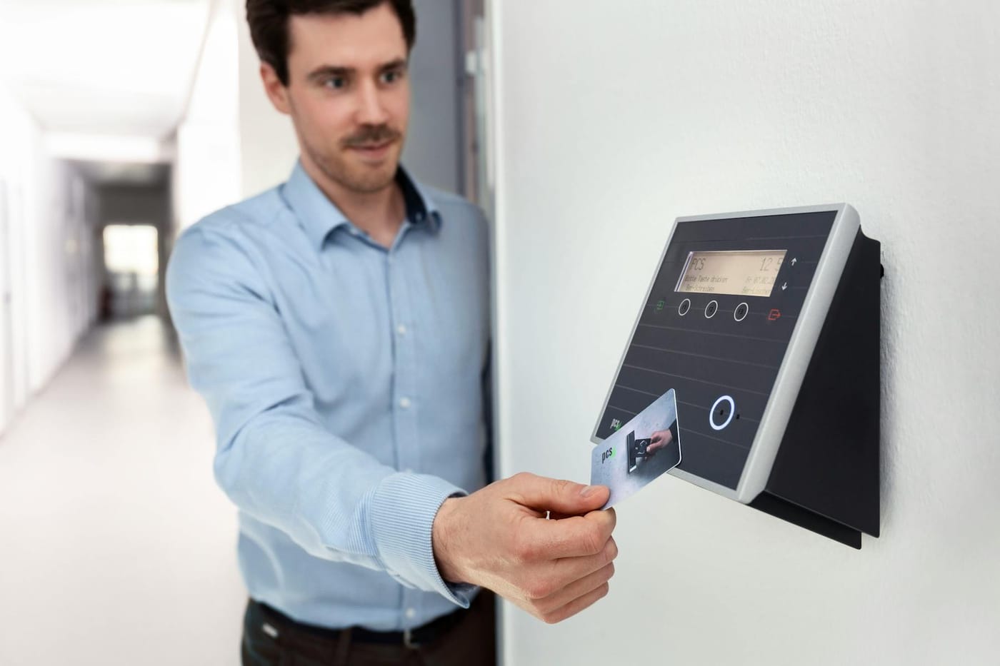 Professional man in shirt holding access card over reader in office corridor