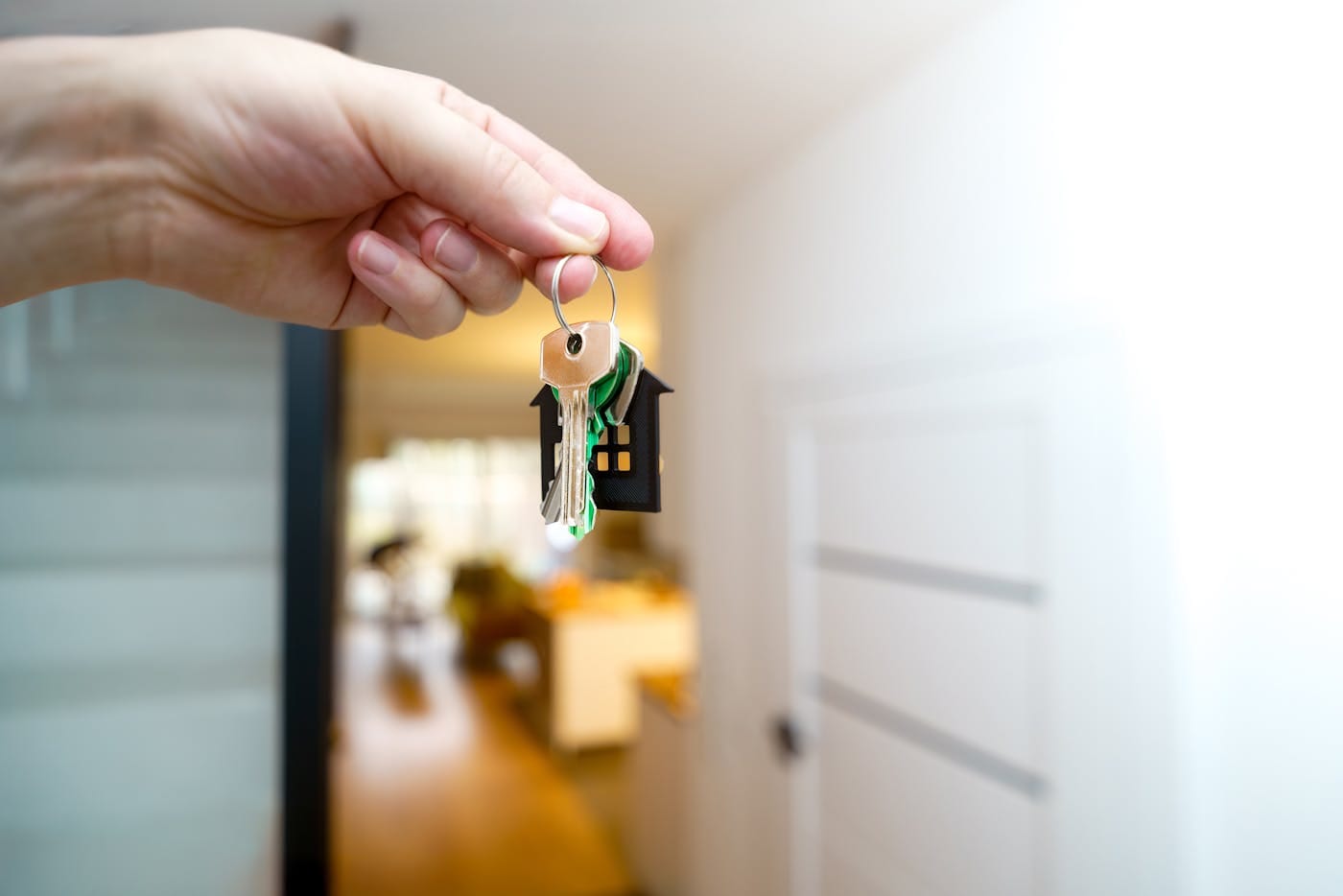Hand holding new home keys with house keychain at residential doorway representing move-in security