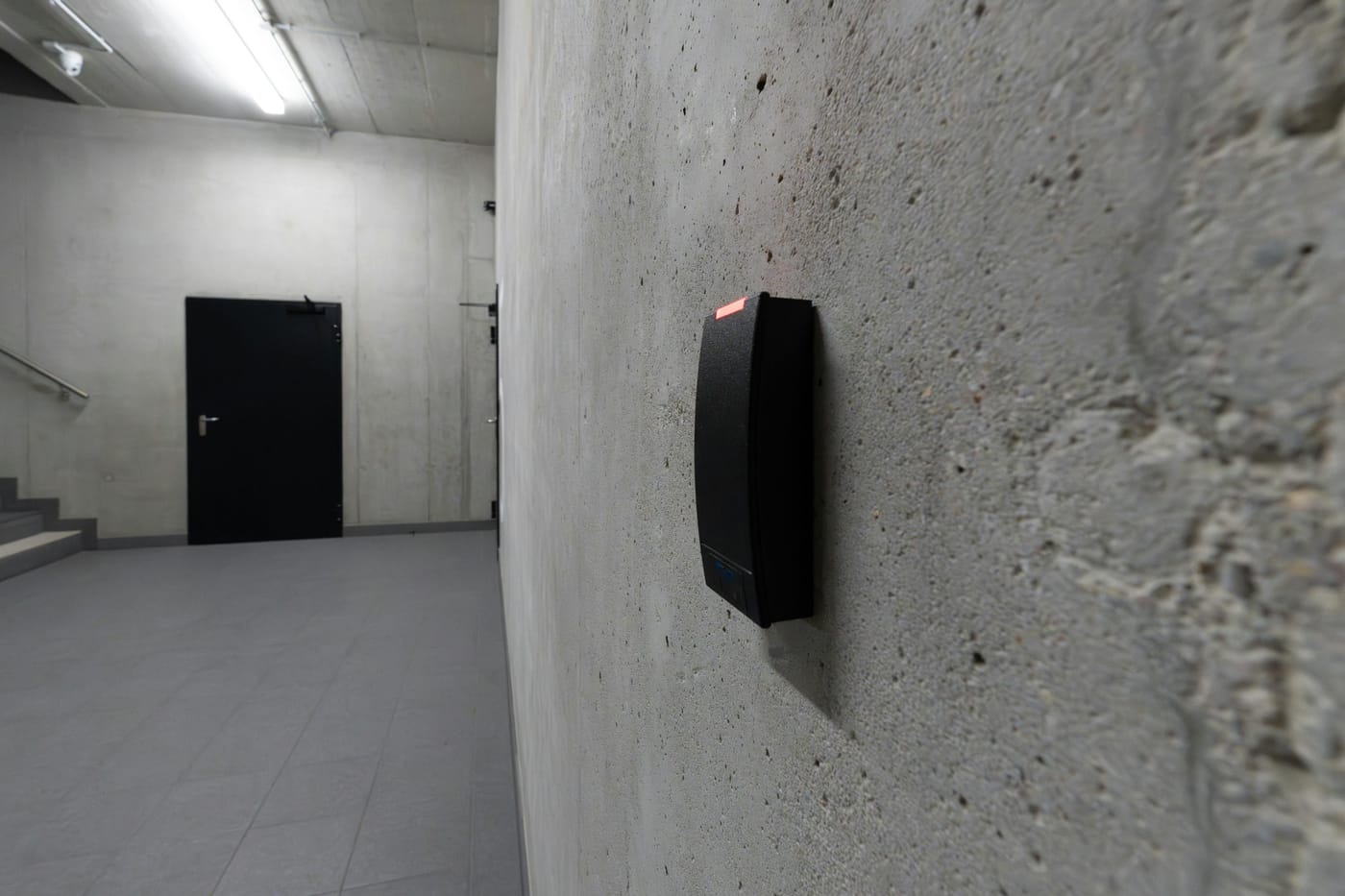 Smart electronic access terminal with proximity card reader mounted on a concrete wall in an industrial corridor