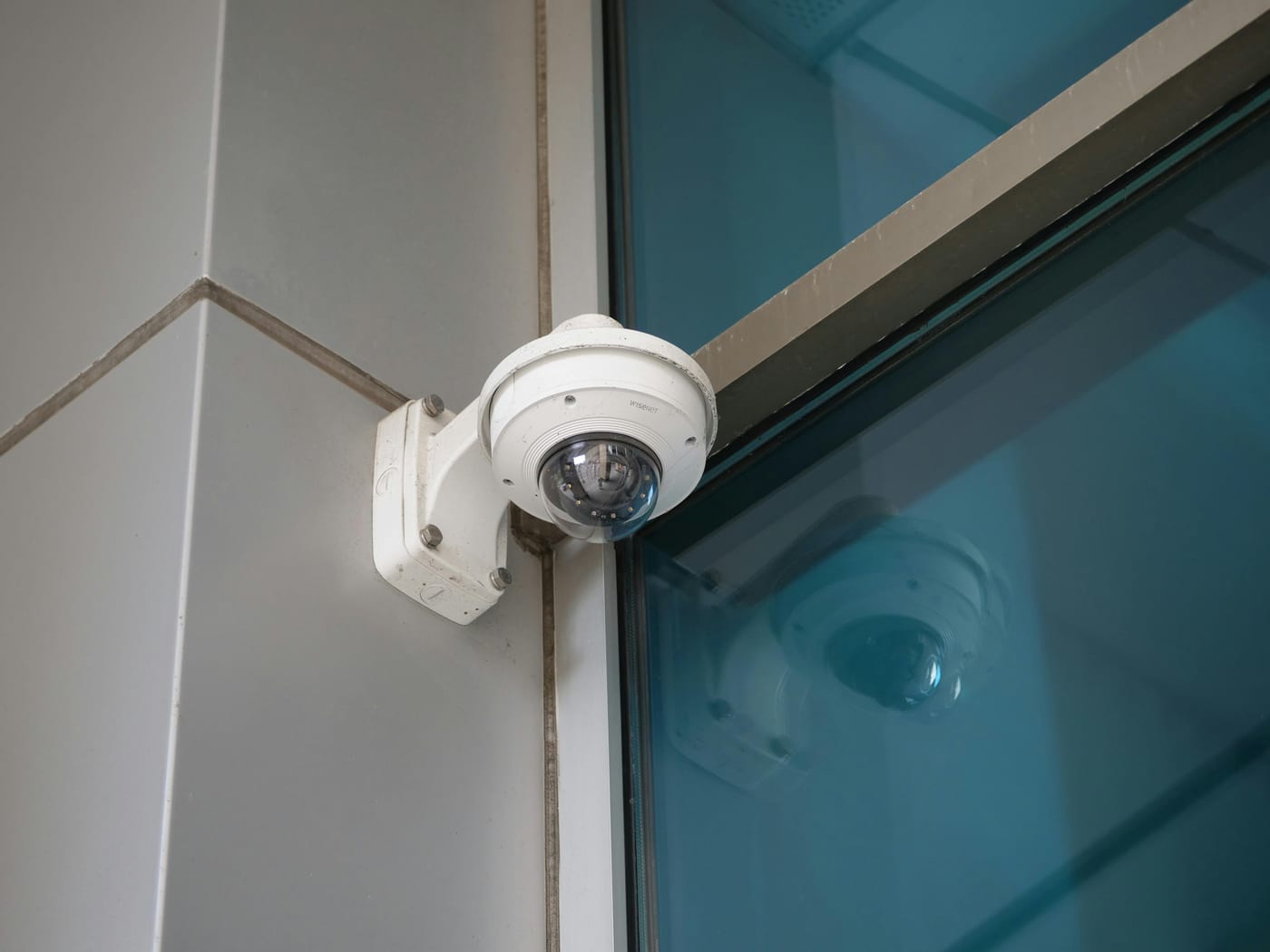 Dome security camera mounted at the glass entrance of a commercial building representing retail surveillance and loss prevention