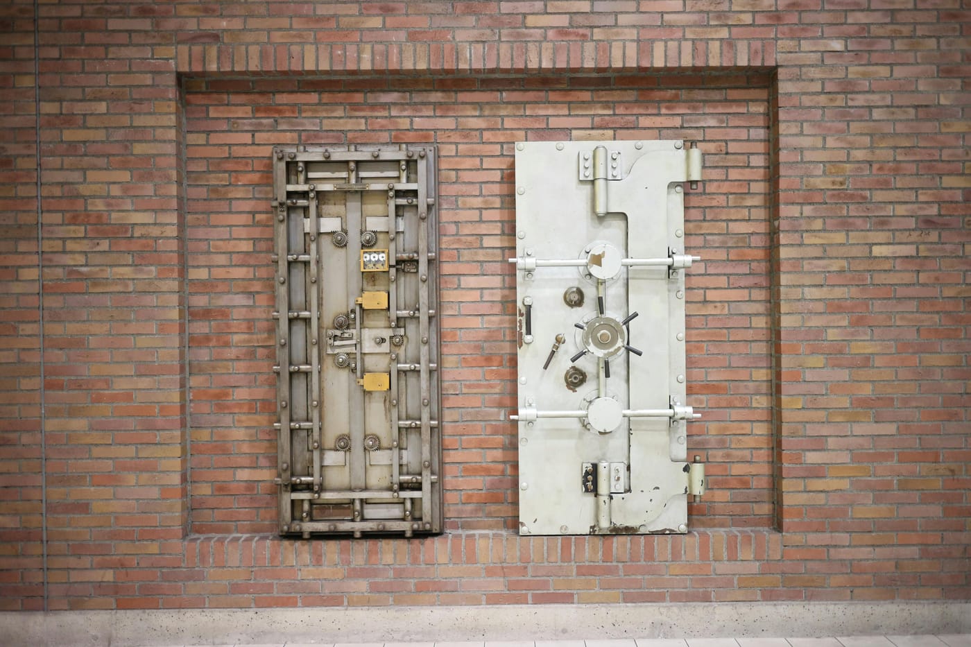Two heavy steel vault doors mounted in a vintage brick wall showing institutional-strength secure storage