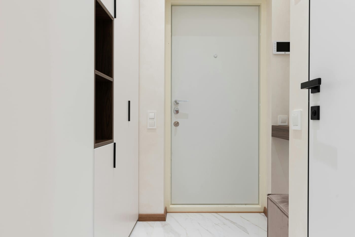 Modern residential apartment entryway with a white steel security door and smart access control panel on the wall beside it