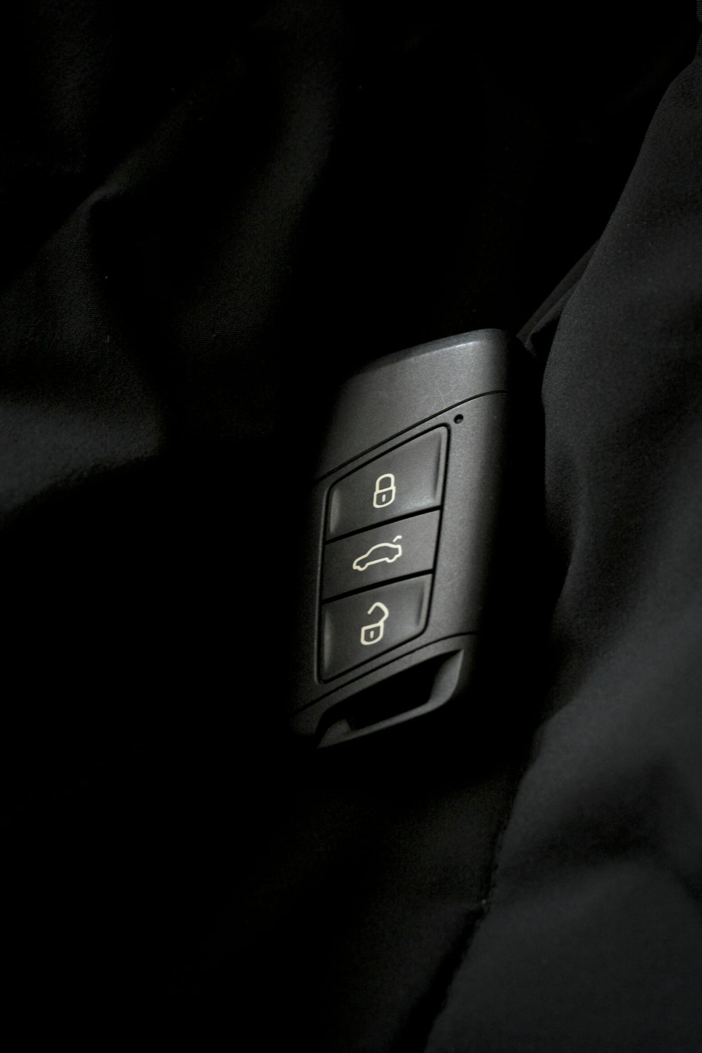 Modern smart car key fob with lock and unlock buttons on black surface for transponder key programming guide. DC Local Locksmith