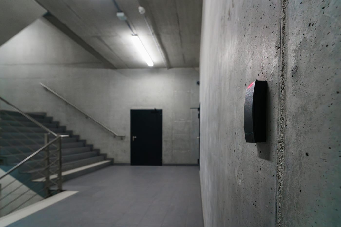 Modern industrial concrete staircase in a commercial office building with a black card access reader mounted on the wall - representing the kind of multi-floor commercial space requiring a tiered master key system
