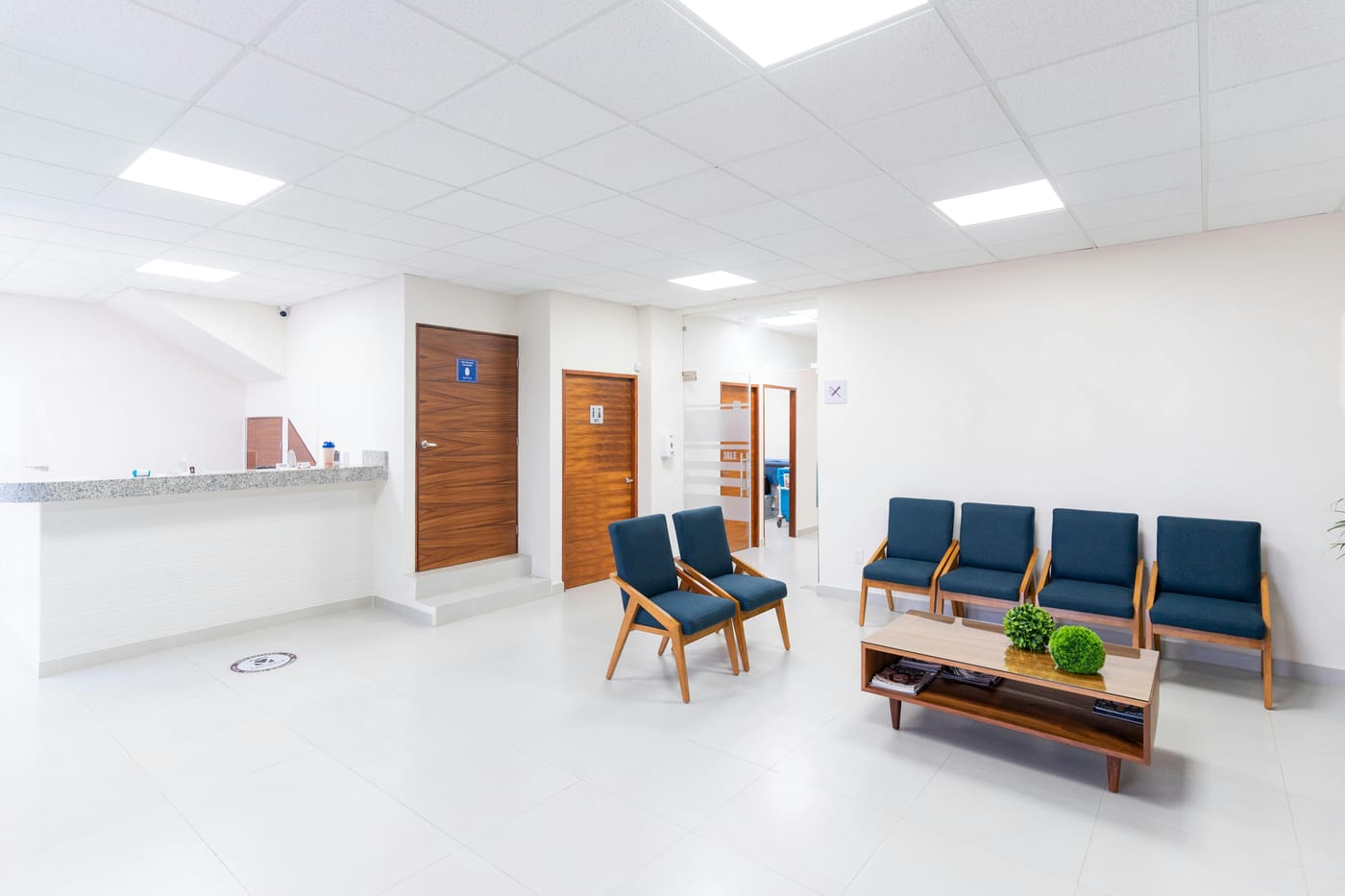 Bright modern medical clinic waiting room with reception desk, wooden doors, and blue chairs - the type of family practice facility requiring HIPAA-compliant access control on patient records rooms