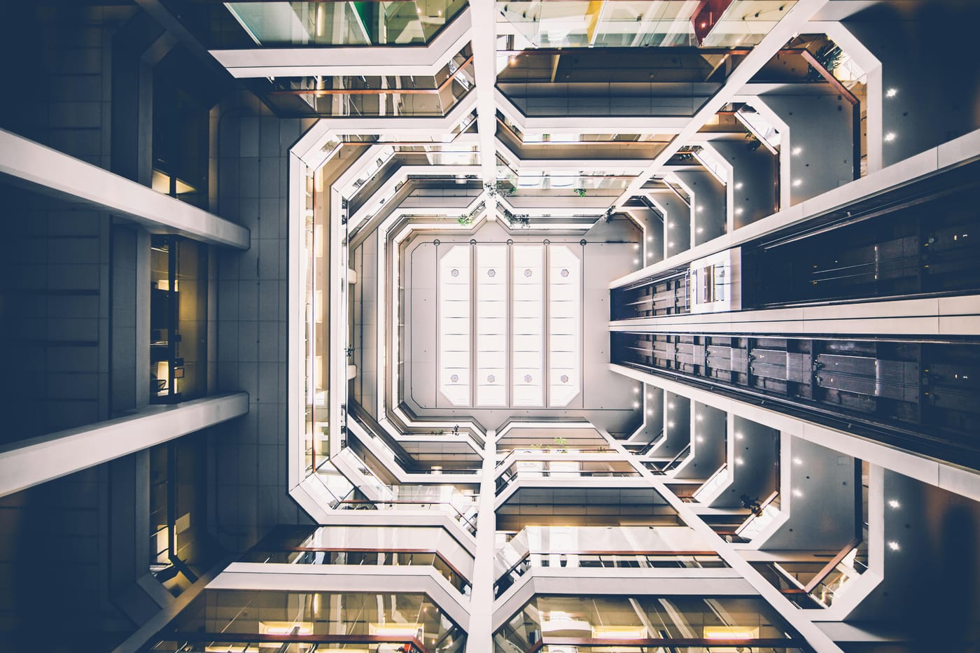 Looking upward through a multi-story commercial office building atrium with geometric balconies and recessed lighting on every floor