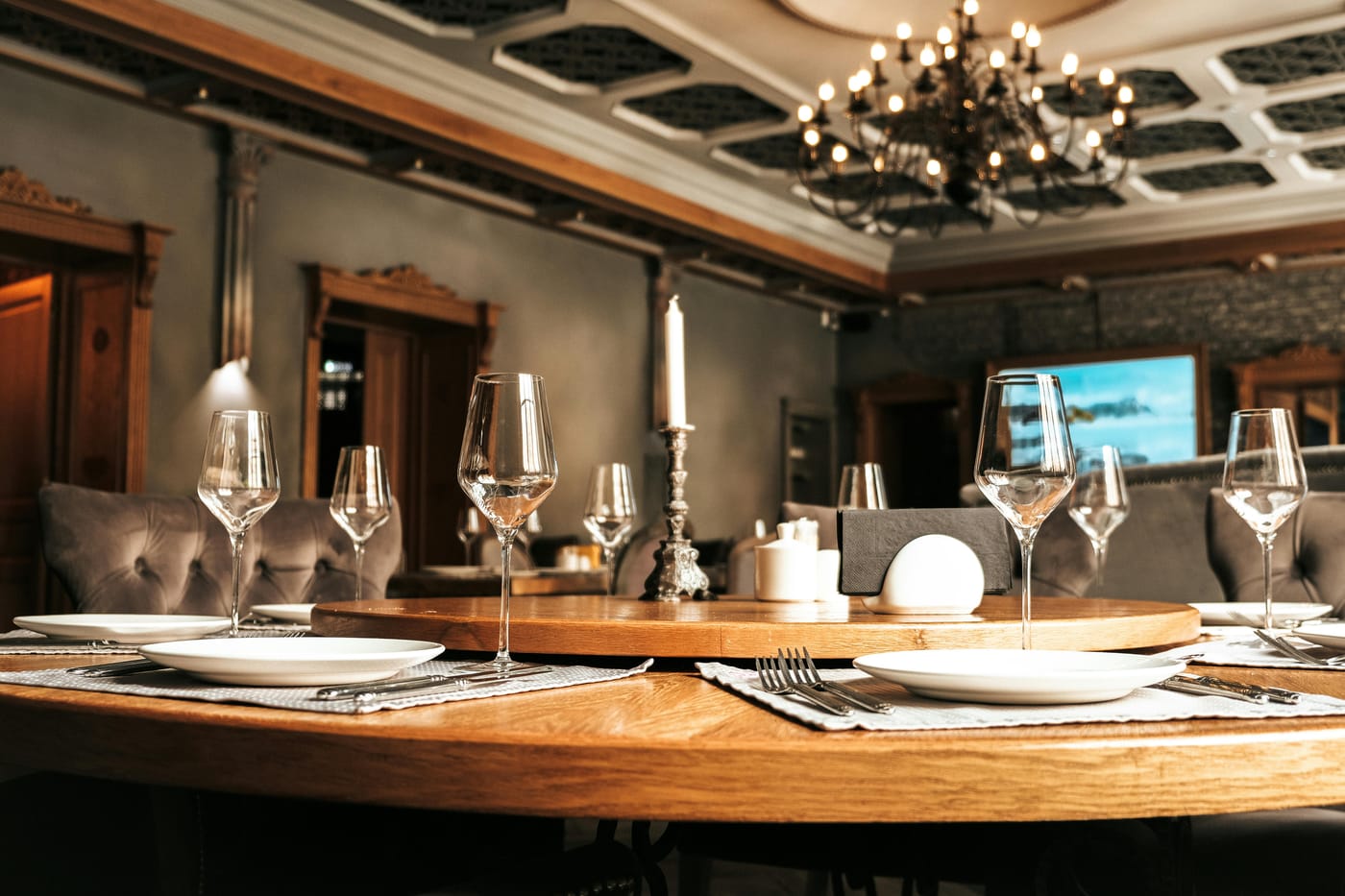 Upscale restaurant dining room with a round table set with wine glasses and white plates beneath a wrought iron chandelier