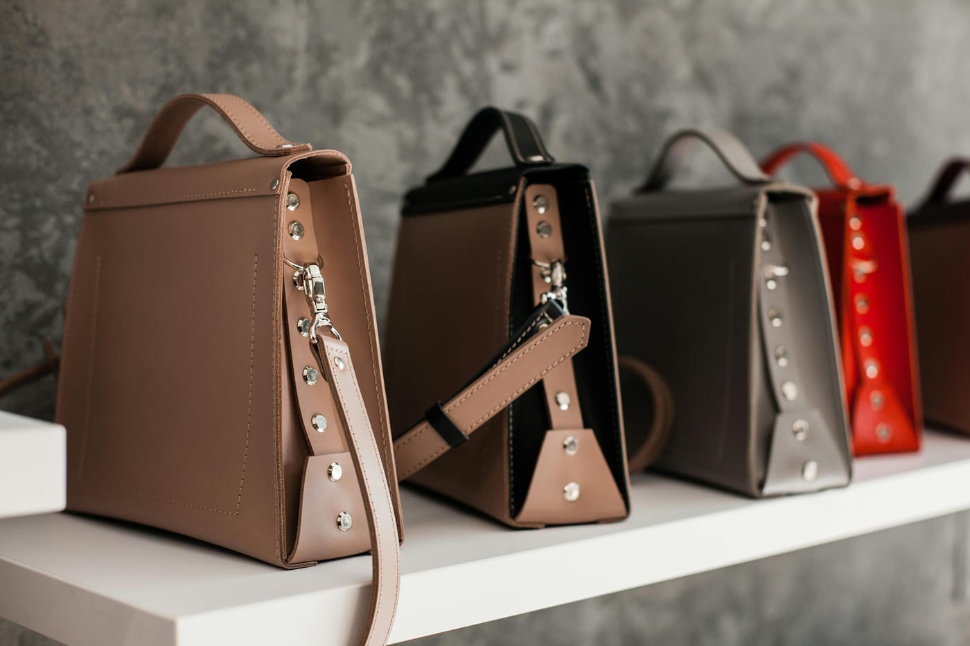 Three high-end leather handbags displayed on a white shelf against a grey concrete wall in a luxury retail boutique