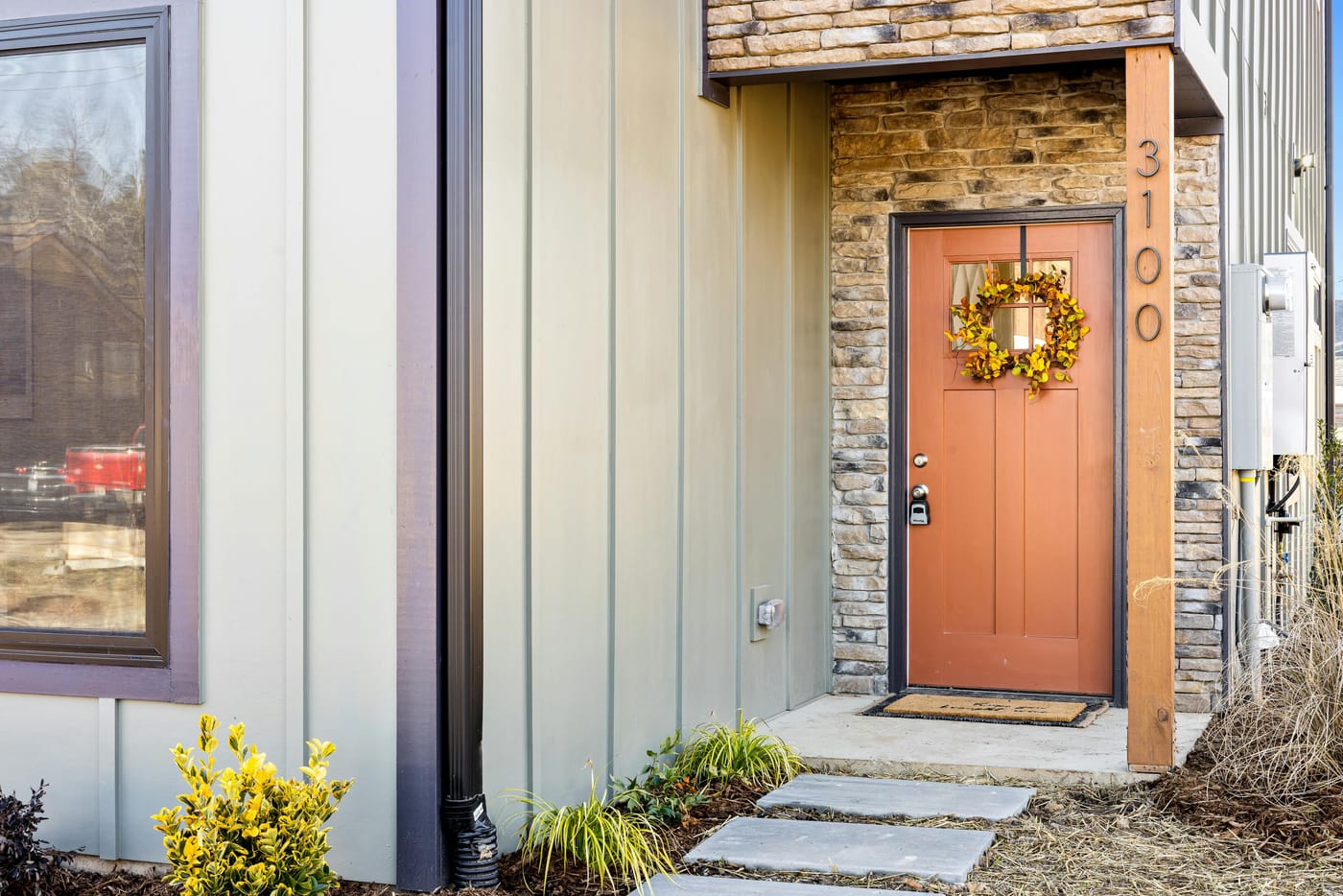 Wooden front door with a wreath beside stone and painted siding