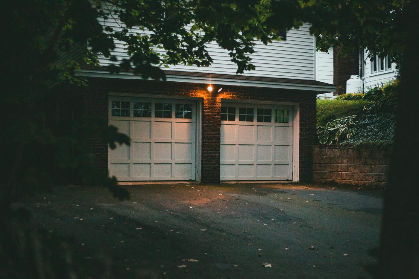 Two residential garage doors under leafy trees