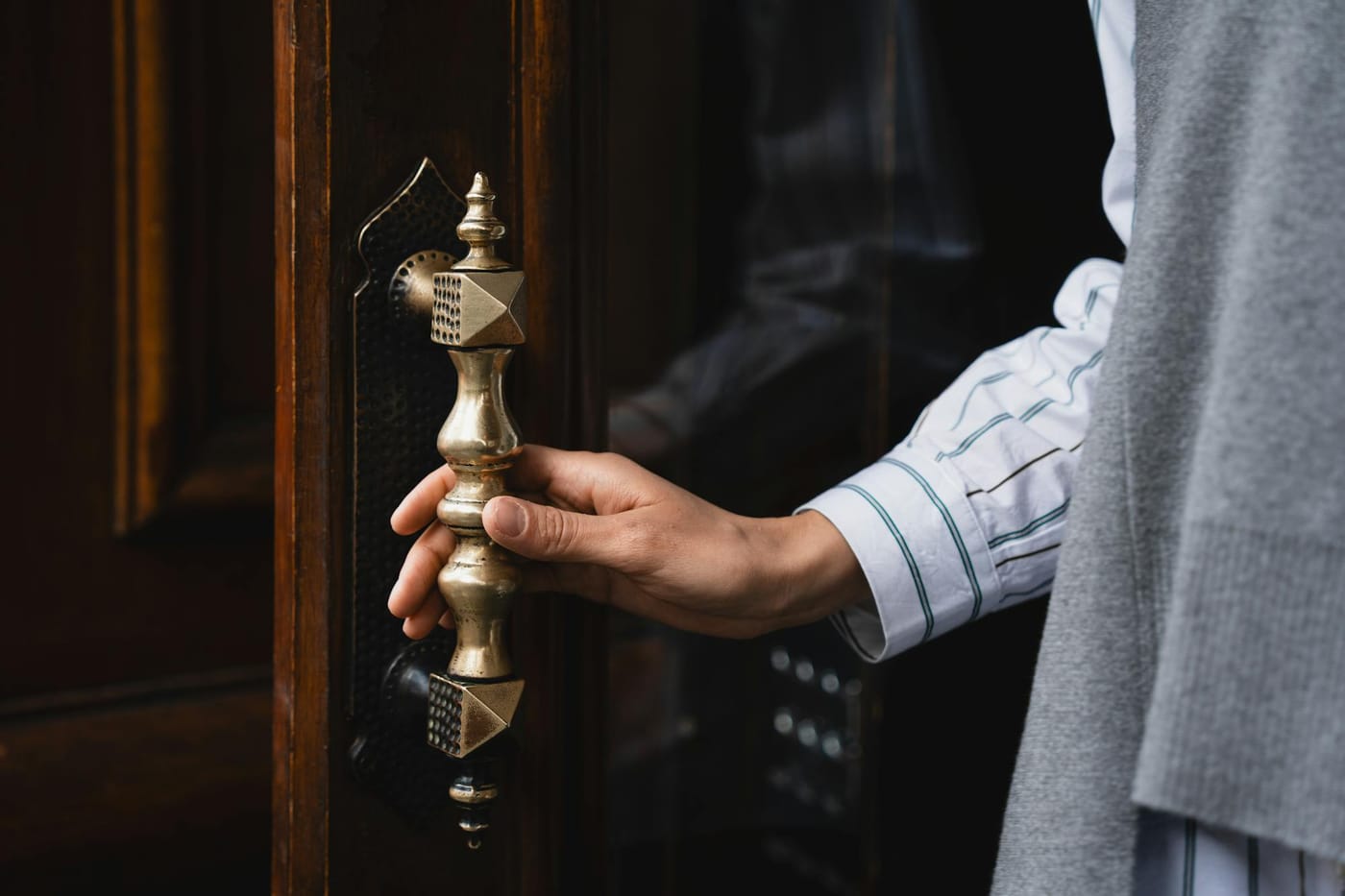Hand holding an ornate brass door handle
