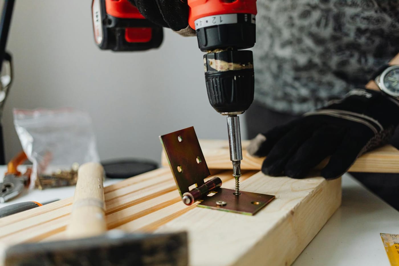 Cordless drill fastening a brass-colored hinge to wood