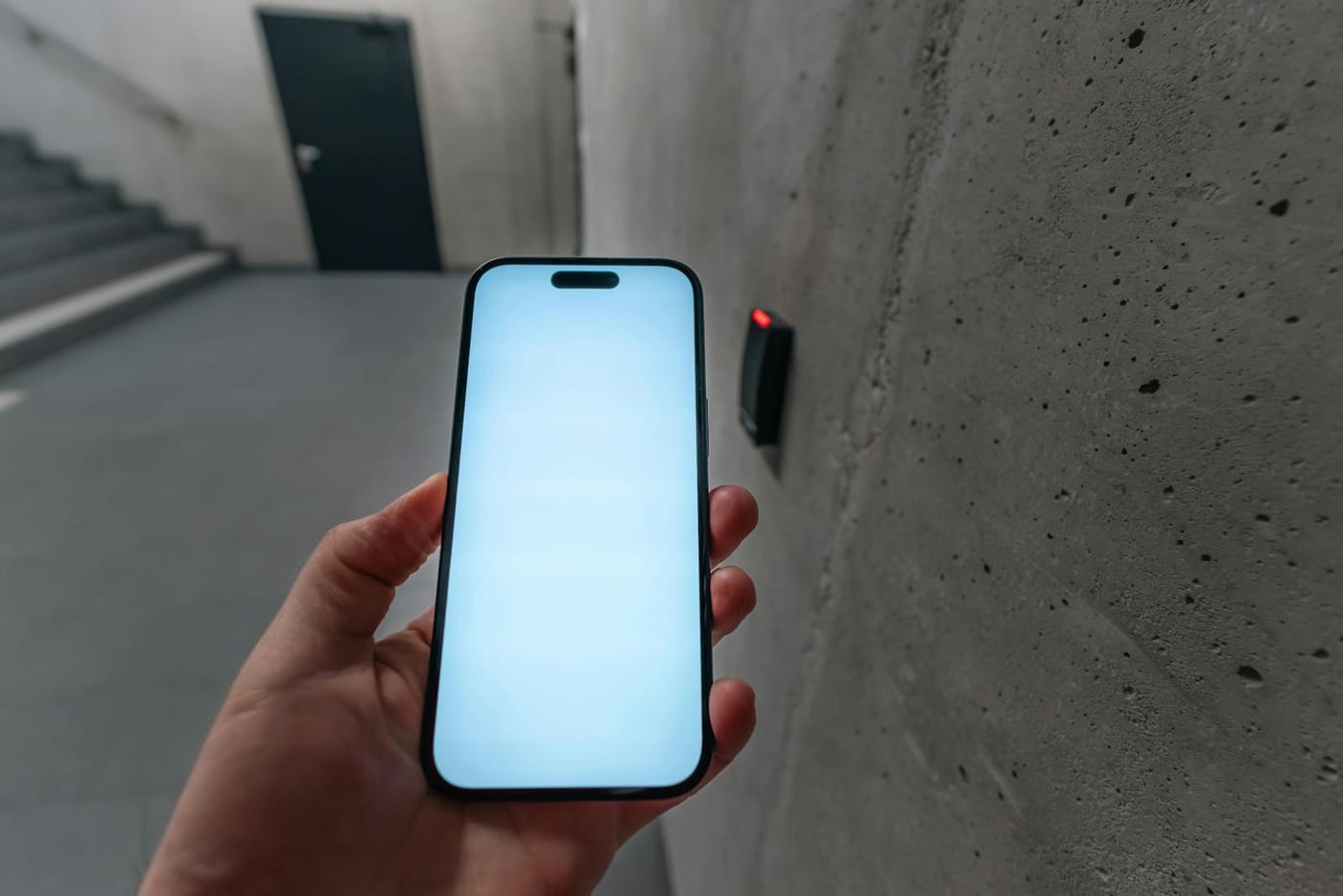 Hand holding a smartphone near a wall-mounted access reader