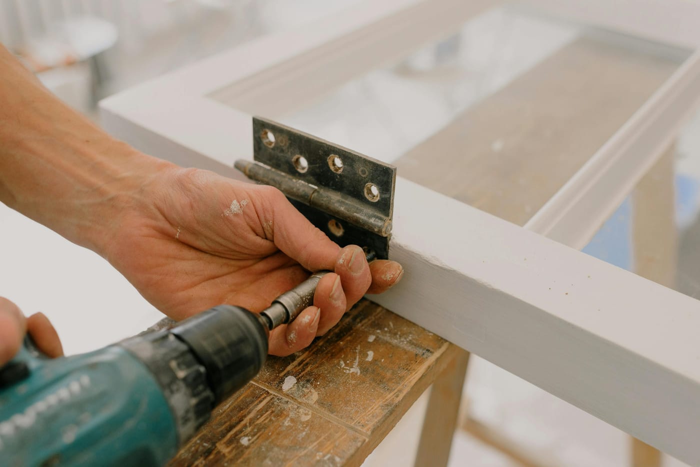 Hands using a drill to fasten a door hinge