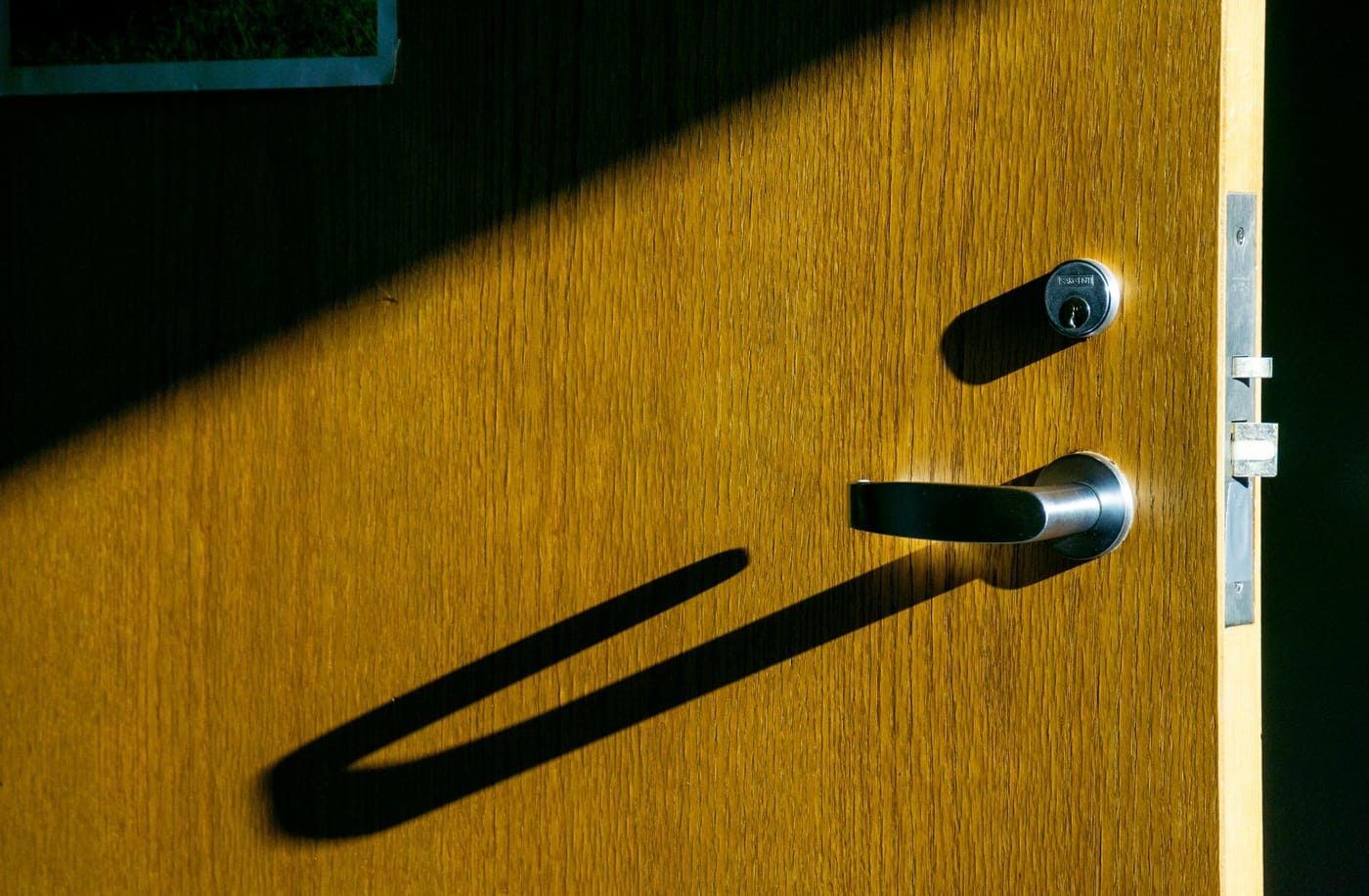 Wooden door with a lever handle casting a long shadow