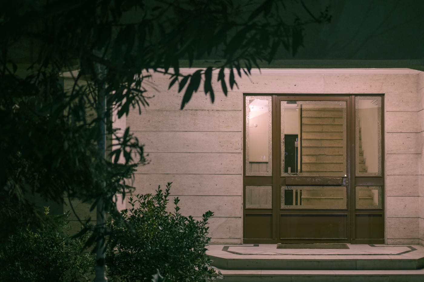 Modern building entrance with glass doors lit at night through foliage for weekend after-hours locksmith service in Washington DC