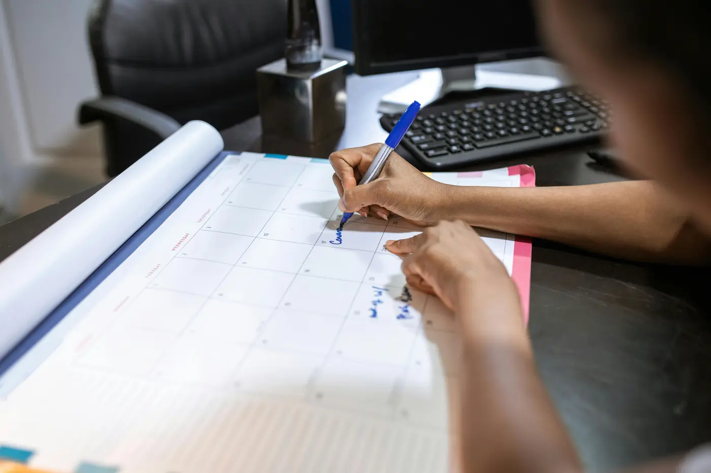 Close-up of a person writing on a large desk calendar, scheduling a locksmith service appointment in a professional office setting