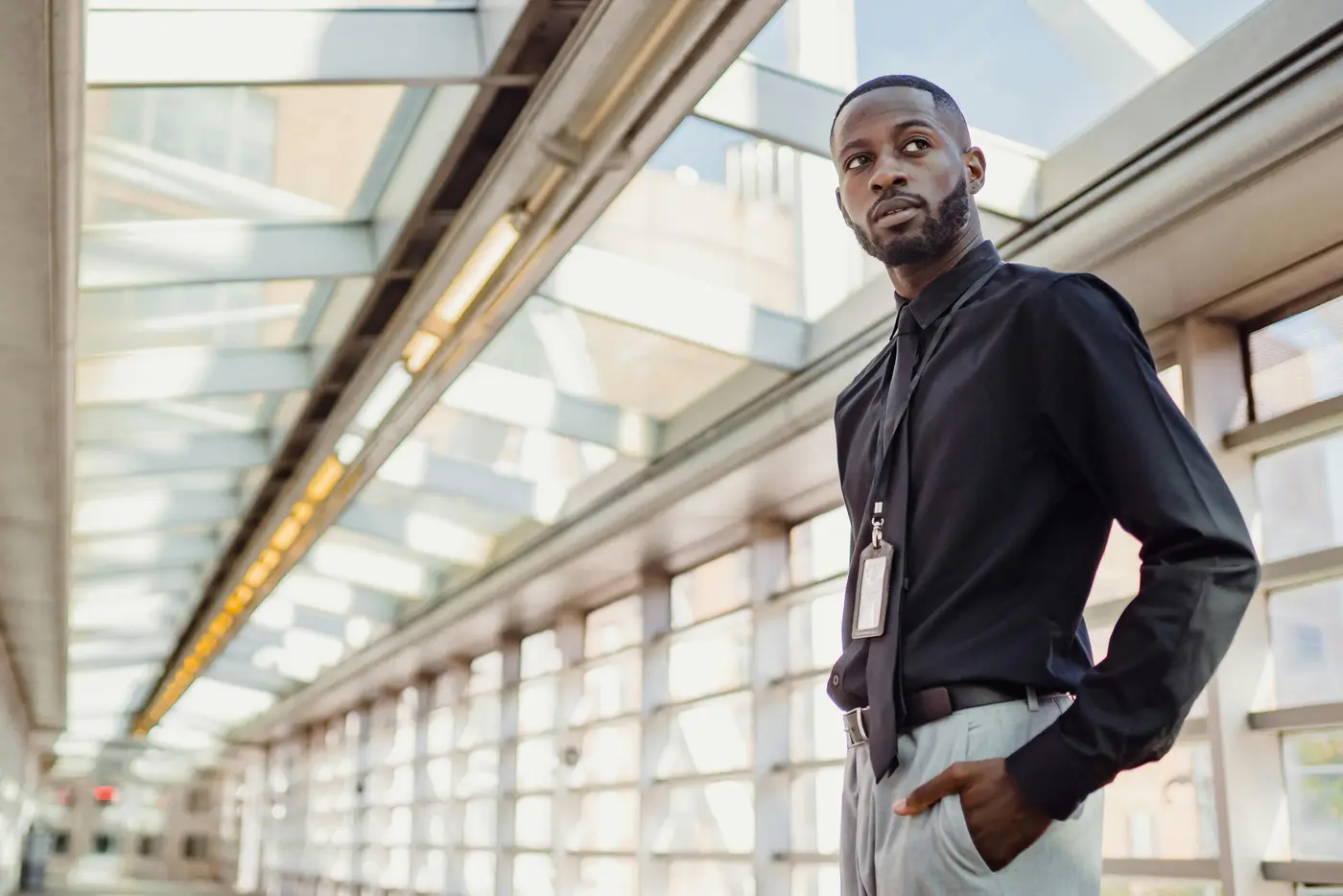 Composed professional in a dark uniform shirt with credential badge lanyard standing in a modern institutional building, representing the licensed and certified expertise of DC Local Locksmith technicians