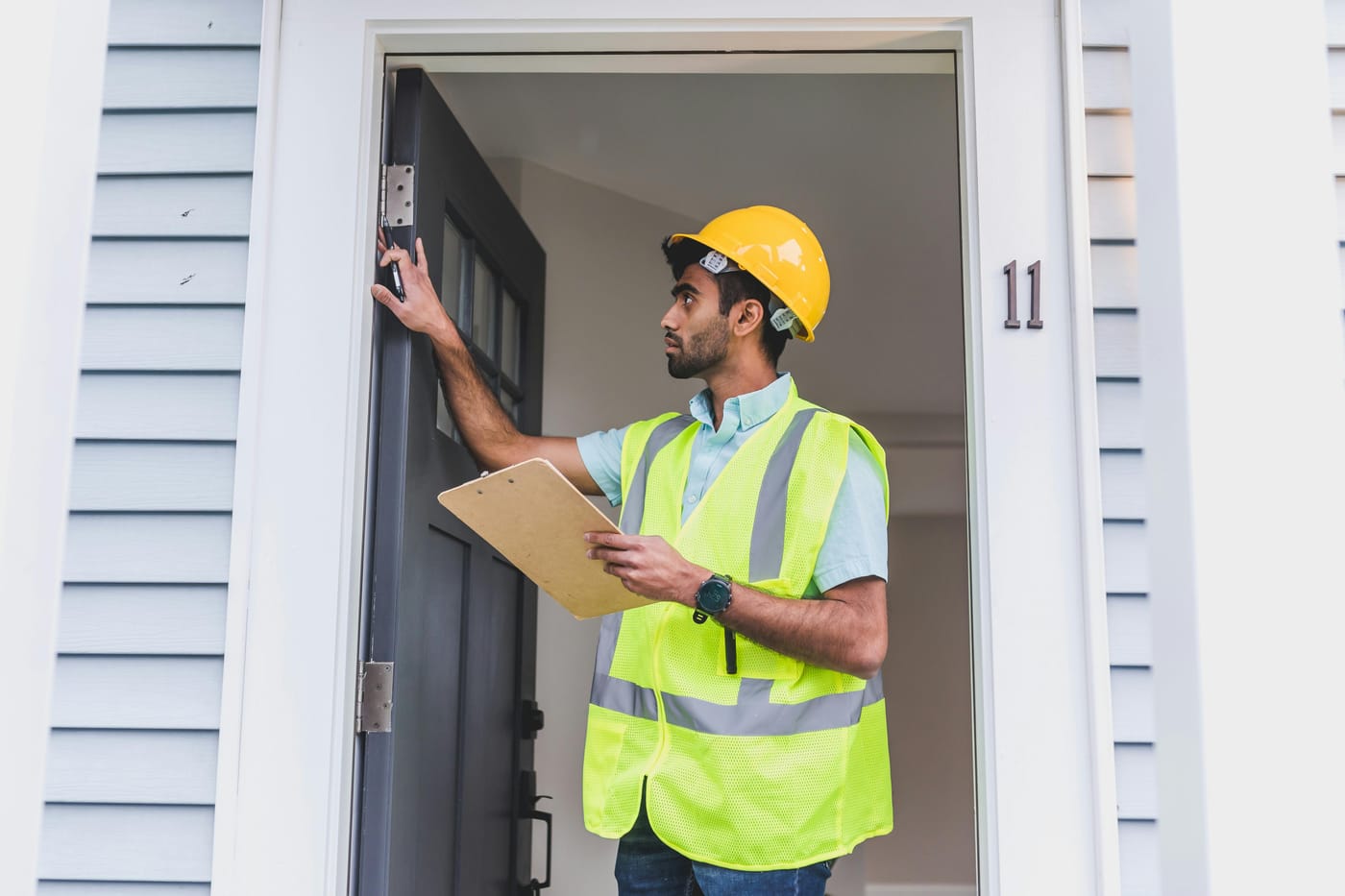 Man in a hard hat examining a doorway while holding a clipboard
