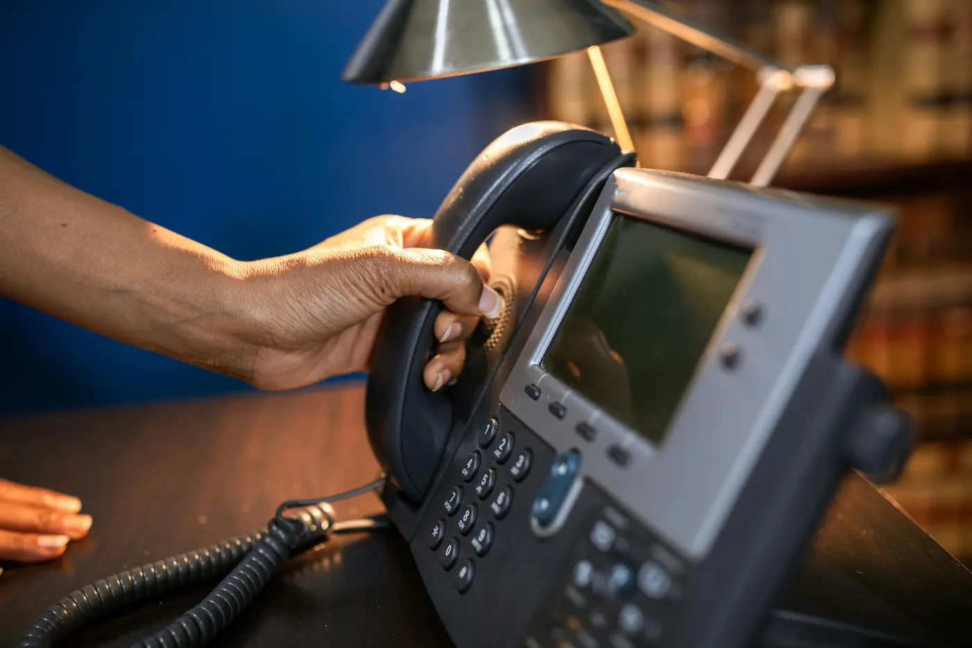 Hand picking up a professional desk telephone with warm lamp light in an office, representing DC Local Locksmith dispatch responding immediately to an emergency quote request
