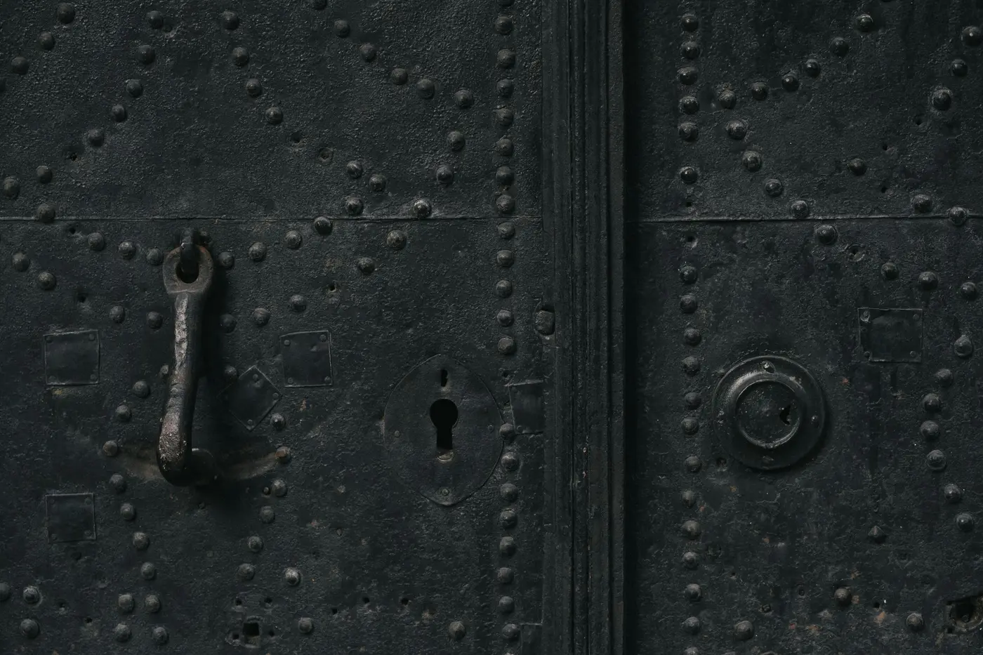 Aged cast-iron gate with ornate riveted panels and a classic lever keyhole, representing the enduring strength and institutional dignity of high-security hardware installations