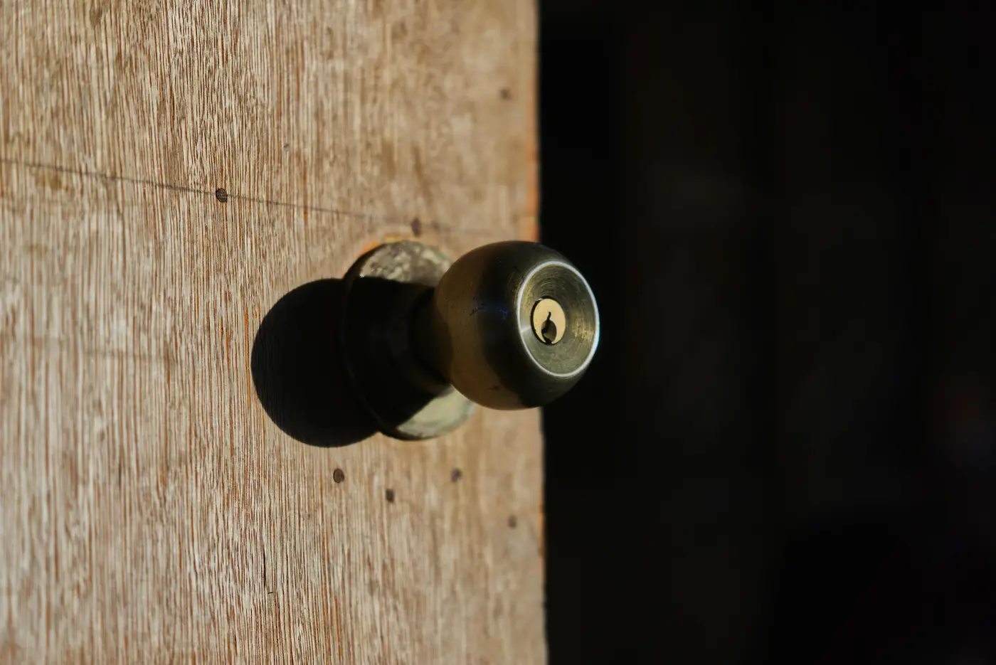 Antique brass door knob with visible keyhole mounted on weathered white-painted wood trim, representing the importance of choosing quality residential lock hardware