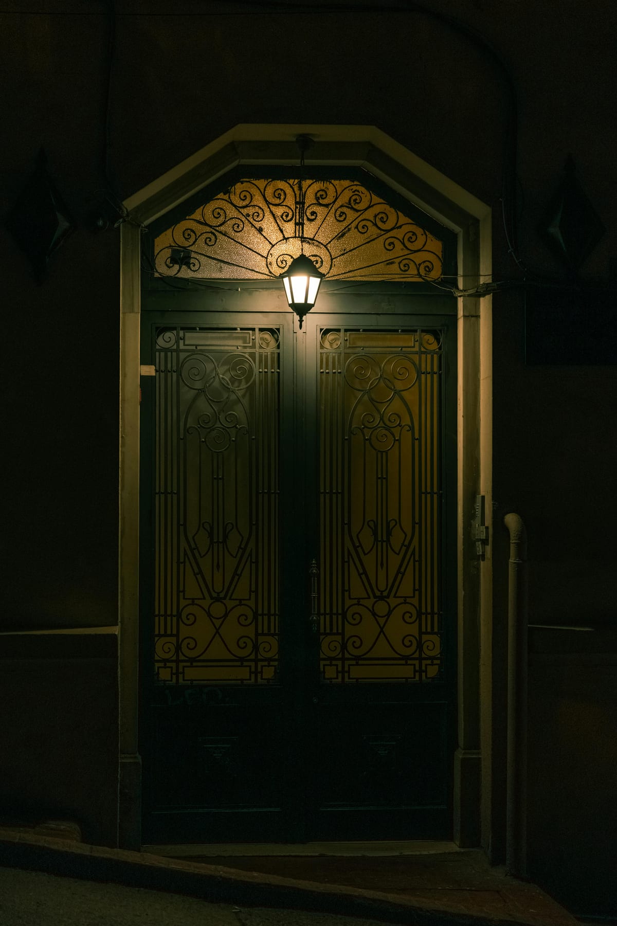 Ornate iron entry door at night with warm interior light visible through glass