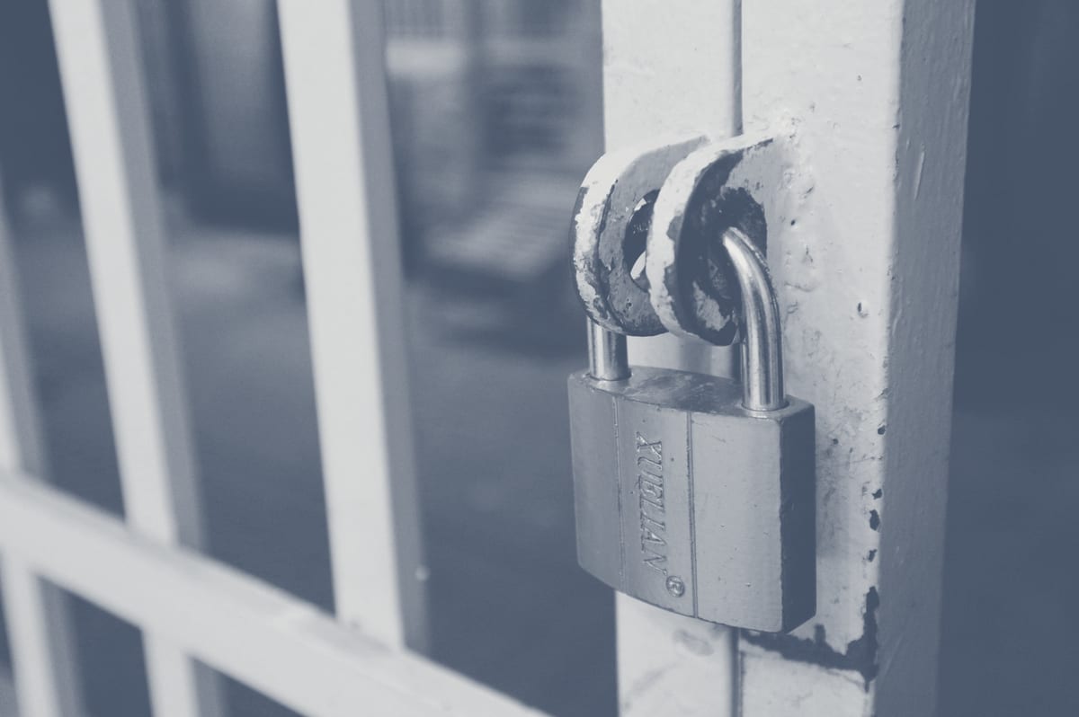 Brass padlock securing a white gate, close-up detail